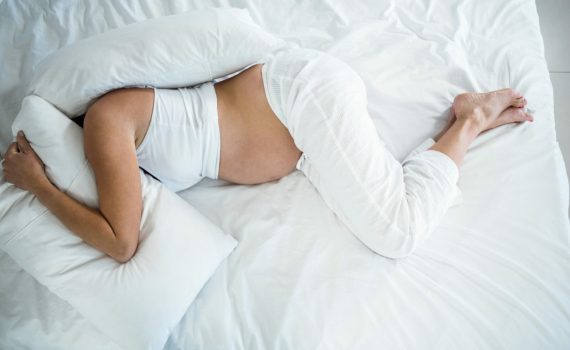 High angle view of pregnant woman with head under pillow on bed
